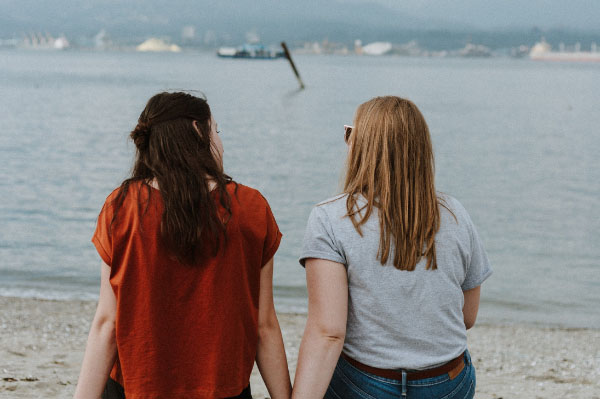 Two women sit talking with their backs to camera