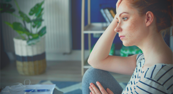 Image of woman at home, sitting on a sofa and looking into the distance