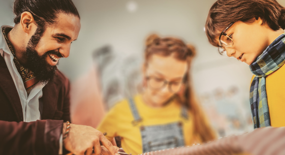 A male youth worker smiles while working with two teenagers.