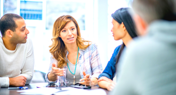 A group of four people sit around a table while having a discussion.