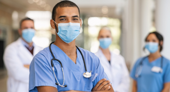 A male nurse in uniform stands in front of a female nurse and two doctors in white coats, all wearing facemasks for infection control during the pandemic.