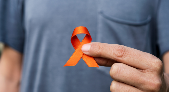 Self-injury awareness: a man holds an orange ribbon symbolizing self-harm awareness to camera