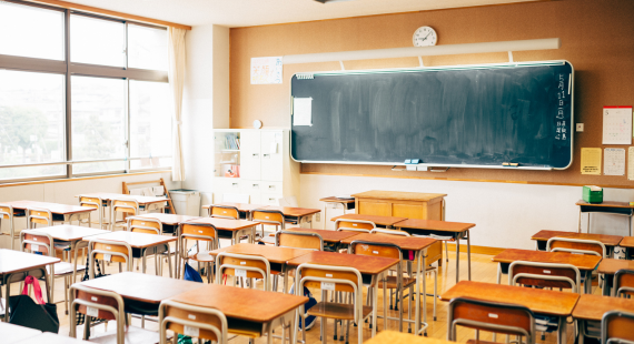 Photograph of a primary school classroom, showing rows of desks facing towards a teacher's desk with a blackboard behind it